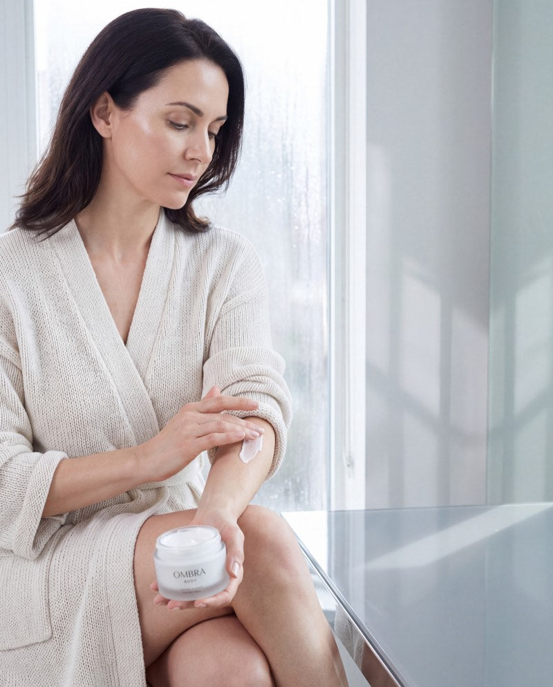 A woman in a robe smoothing cream along her arm.